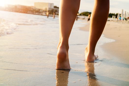 Pretty woman legs walking on the beach. Rear view. Close-up.