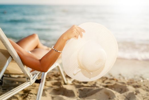 Close-up of unrecognizable female person with white summer hat  enjoying on the beach. 
