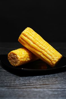 Two corn cobs on black plate against dark background