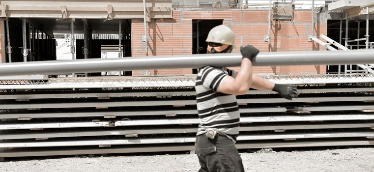 Builder worker with a long pipe on the shoulder at building construction site, France