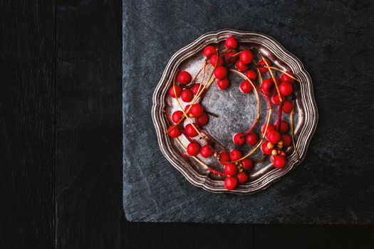 Red berries sprig in the vintage metal plate on the black stone