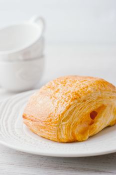 Cream puff on the white plate with two blurred cup at the left