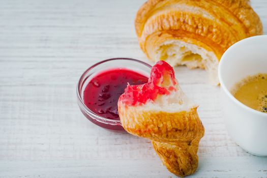 Croissant dipped in berry jam with cup of coffee