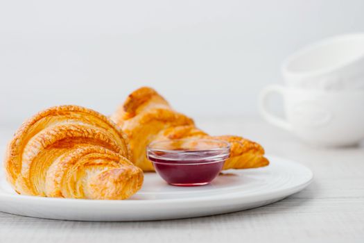 Croissants with berry jam and two white blurred cups horizontal