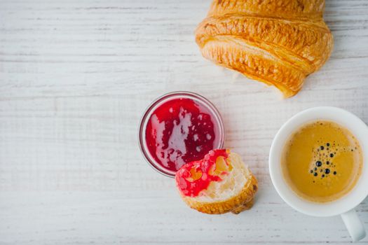 Croissant dipped in berry jam with cup of coffee top view
