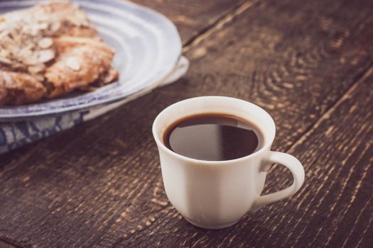Cup of coffee with blurred croissant   on the blue ceramic plate horizontal