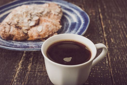 Cup of coffee with blurred croissant  with almond on the blue ceramic plate