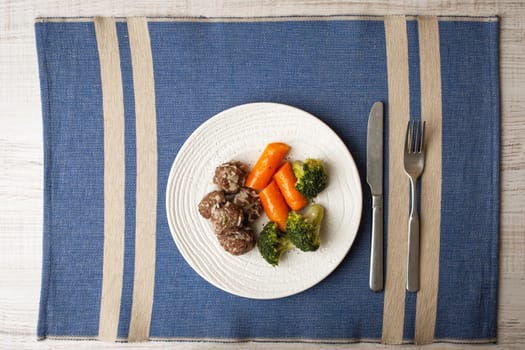 Steamed meatballs and vegetables on the blue napkin with cutlery top view