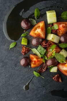 Vegetable salad with dried tomatoes and olive on the black stone vertical