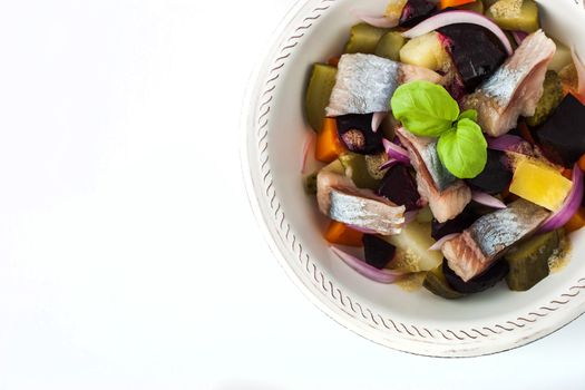 Vegetable salad with herring on the white ceramic dish  top view