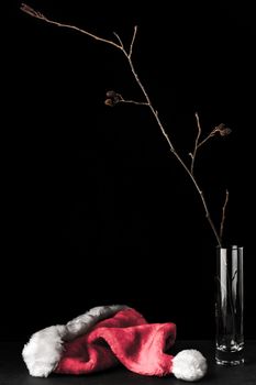 Alder branch in the glass and santa claus hat on the black stone table vertical