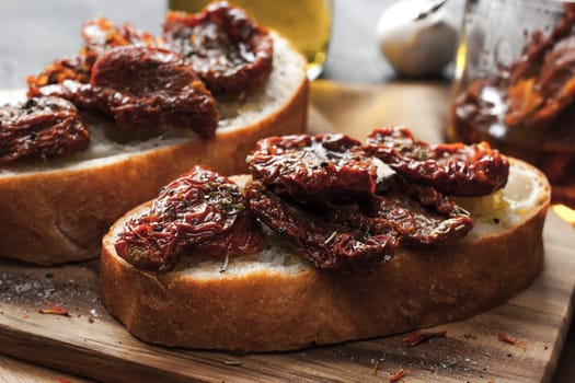Sun-dried tomatoes on the white bread on the wooden board horizontal