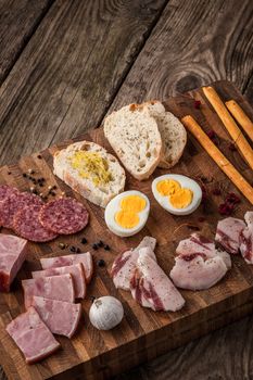 Eggs, ham, sausage, bread, pepper, garlic on a cutting board vertical