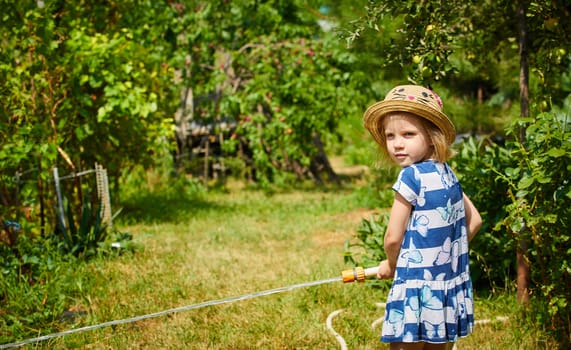 Little happy girl watering garden. Summer day