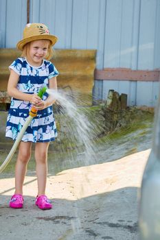 Little girl in hat watering lawn. Summer day