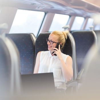 Businesswoman talking on cellphone and working on laptop while traveling by train. Business travel concept.