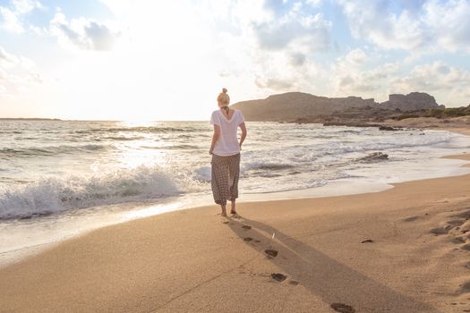 Woman walking on sand beach at golden hour. Seashore sunset walk.