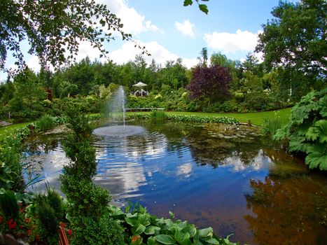 Ornamental pond and water fountain in a beautiful creative lush green blooming garden