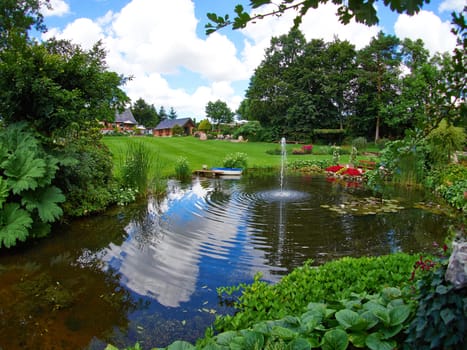 Ornamental pond and water fountain in a beautiful creative lush green blooming garden