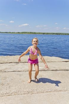 Dancing girl on the riverbank in pink swimsuit
