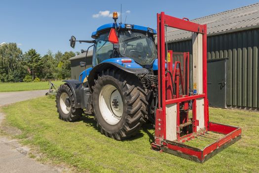 Blue tractor with a red bale slicer for cutting off silage bales
