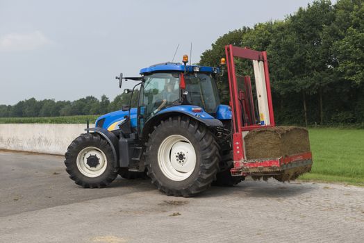 Blue tractor with a red bale slicer for cutting off silage bales
