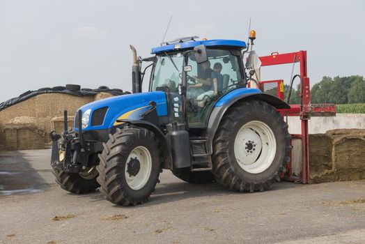 Blue tractor with a red bale slicer for cutting off silage bales
