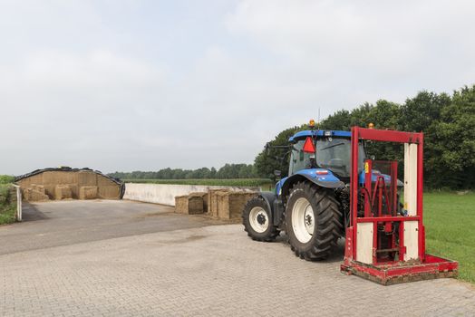 Blue tractor with a red bale slicer for cutting off silage bales
