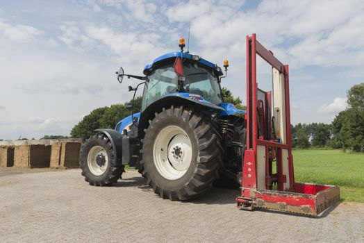 Blue tractor with a red bale slicer for cutting off silage bales
