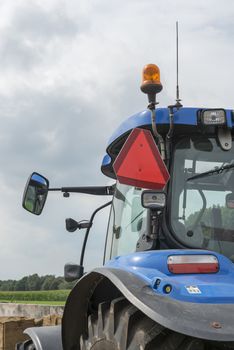 Blue tractor with detail of the truncated warning triangle for motor vehicles with a limited speed on the left side
