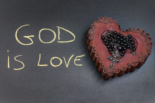 In the picture a rosary iron placed over a heart of red wax, on the left side the inscription "God is Love" made with a crayon.