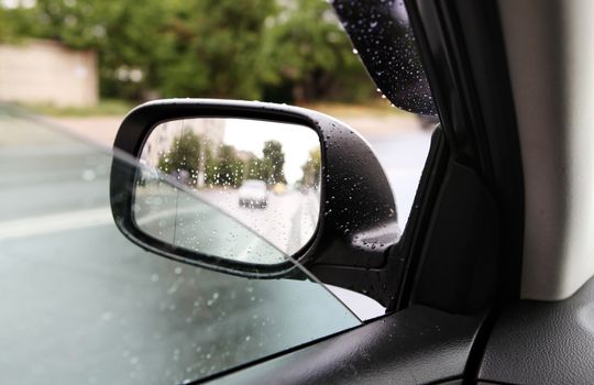 car driving on empty road, rear-view mirror in rainy weather