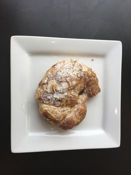 Pastry with nuts on a white plate, sweet croissant.