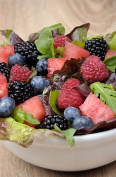 Fruit salad with blackberry, raspberry, blueberry, watermelon slices and mix of green leaves