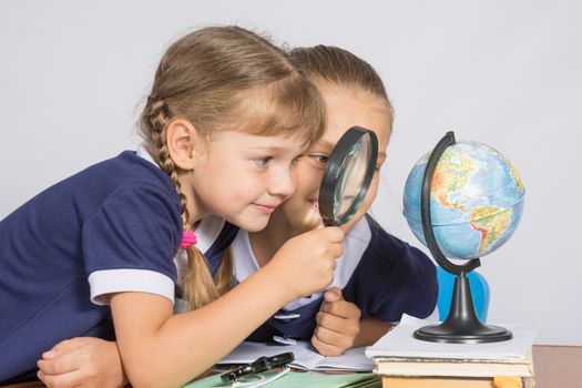 Two girls girlfriends looking at globe through a magnifying glass