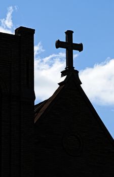 Iron cross on top of a Christain church steeple silhouetted against a blue sky.