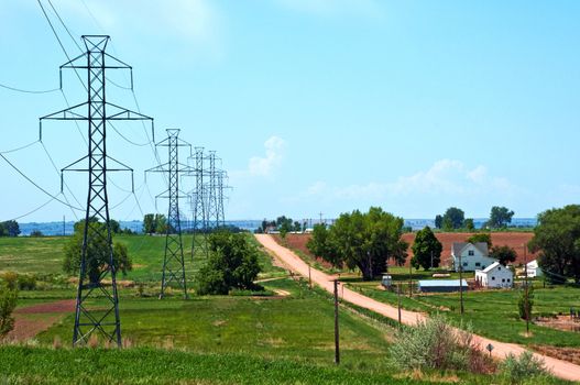 Steel power poles carry electricity through the rural landscape towards a large city.