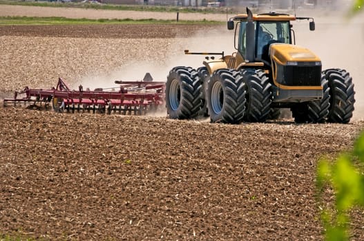 Farmer stirring up dust using a disc harrow to prepare his field for planting.