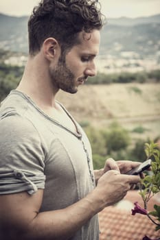 Handsome trendy man using cell phone to type text message outdoor. Side view