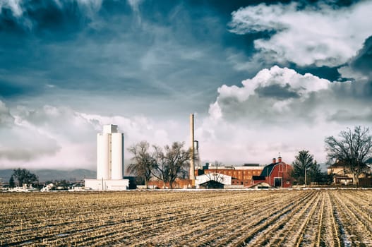 Abandoned sugar mill in a small rual Colorado town against a stormy sky across a fallow field.