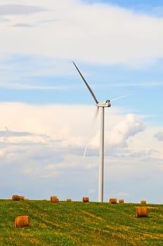 Wind turbines share a field with bales of straw as two renewable resources co-exist on the same land.