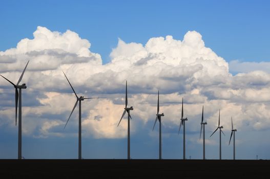 Row of Wind generators silhouetted against large billowing clouds in the evening sky. In central Colorado, USA.