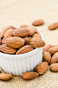 Almond in white bowl on sack background.