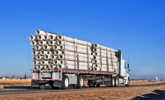 Big truck with flatbed trailer hauling plastic pipe.