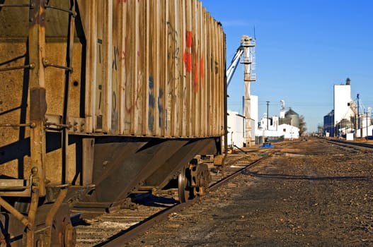 Quiet scene of a rural town with an old rusty railcar covered with graffiti waiting on a rail siding.