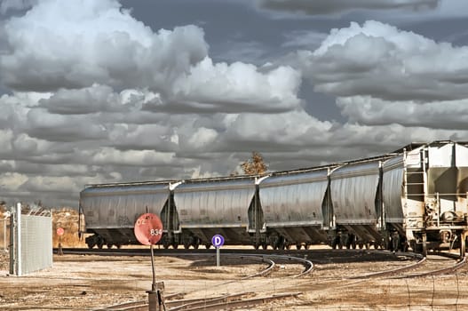 Bulk product railcars waiting thier turn to be loaded under a stormy sky.