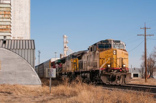 Freight train loaded with automobiles in covered transport cars traveling through a small rural Colorado town in the USA