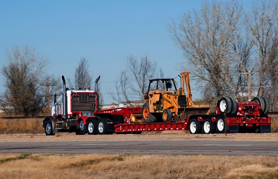 Semi-truck hauling pipeline laying equipment on a drop-deck trailer.