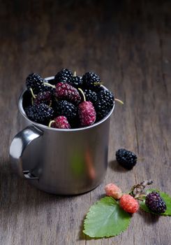 Mulberries in metal mug on wooden background