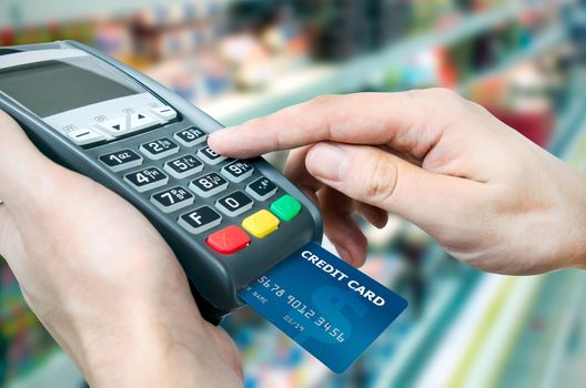 Hand with credit card swipe through terminal for sale in supermarket